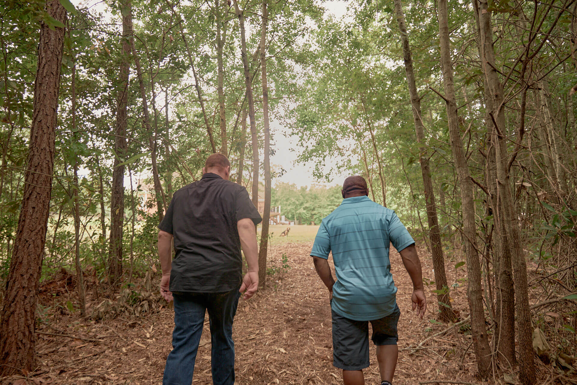 rear view of John and Darrell walking up hill in wooded area