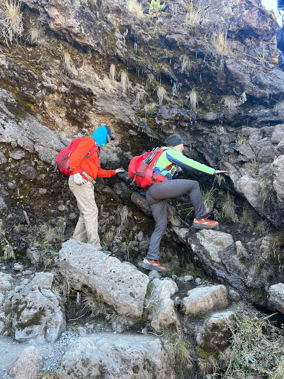 Two climbers navigating a rocky section of the Mt. Kilimanjaro climb