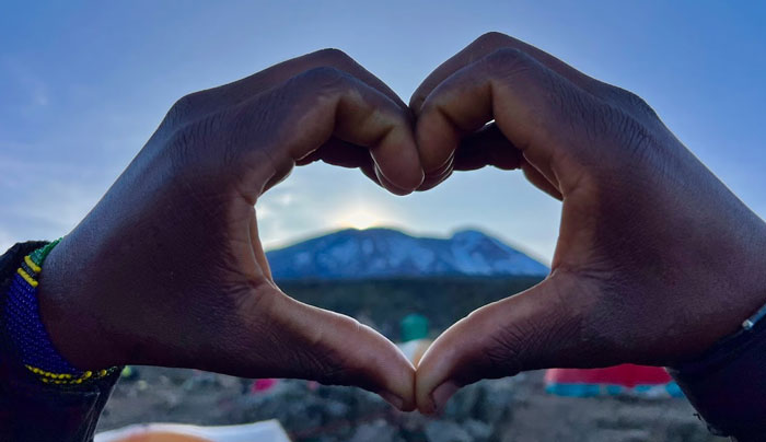 Hands held together in heart shape framing Mt. Kilimanjaro in distance.