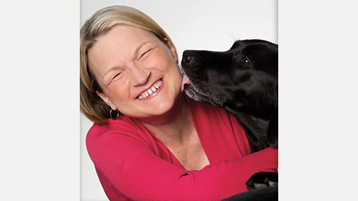 Liza smiling as her dog kisses her