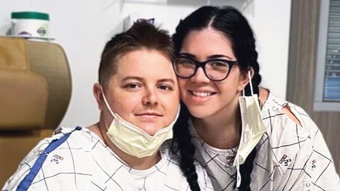 Two individuals wearing hospital gowns, face to face, smiling