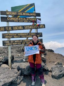 Alaina standing in front of Mt Kilimanjaro summit sign holding a UNOS sign