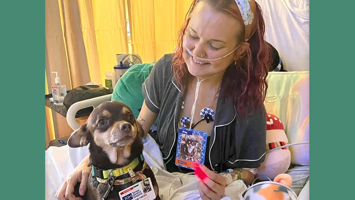 Emma, sitting on hospital bed, smiling, with hand on small dog