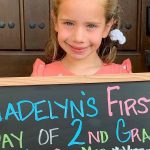 Transplant recipient, Madelyn, holding a chalkboard commemorating her first day of 2nd grade