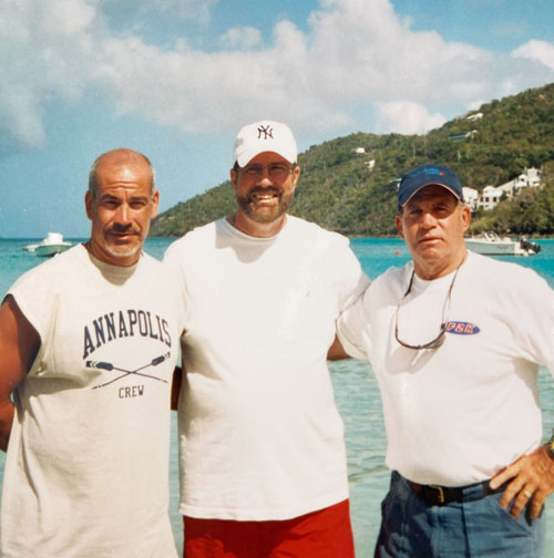 Three brothers standing in a row with beach and hill in background